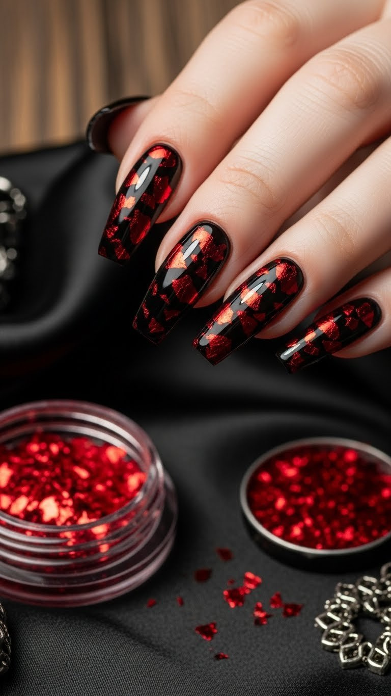 Bold glossy jet black coffin nails with delicate metallic red foil flakes, on black silk scarf, dark wood.