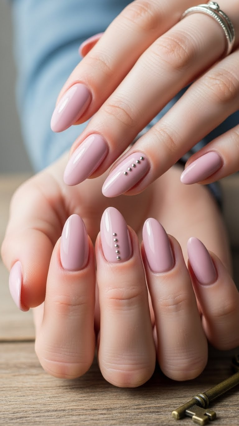 Elegant almond nails in pale pink/mauve with a subtle micro-dot accent on the ring finger, showcasing minimalist nail art.