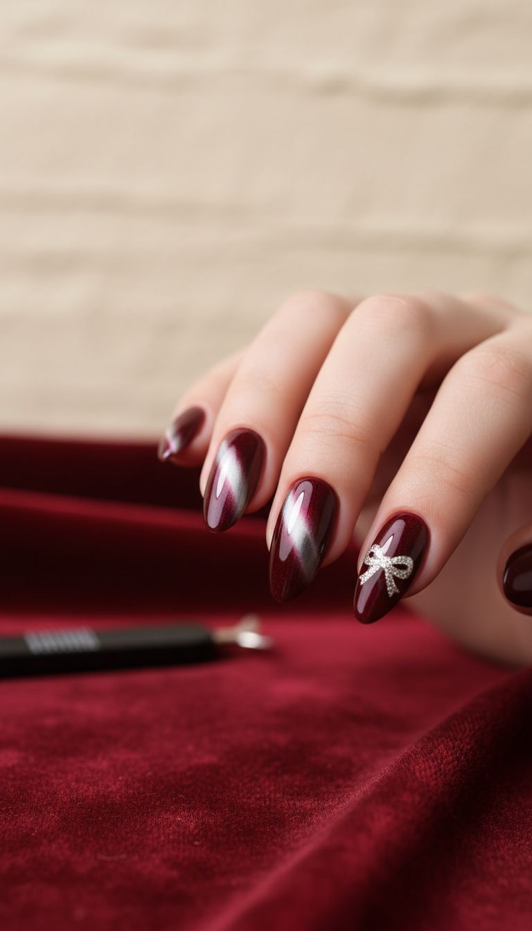 Glamorous burgundy cat eye gel manicure, shimmering magnetic stripe, delicate silver glitter bow on accent nail.