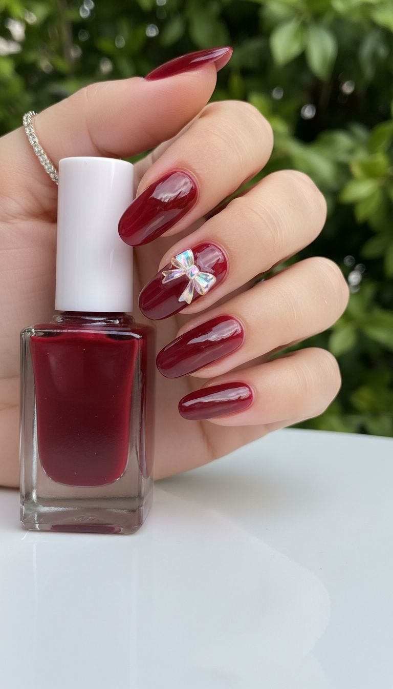 Long oval dark red jelly nails with an encapsulated iridescent bow charm, showcasing glossy translucent finish.