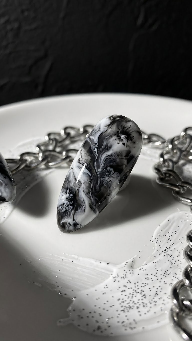 Sophisticated black & white blooming gel nail art: edgy marble pattern on almond-shaped nail. High-contrast gel manicure, modern aesthetic.